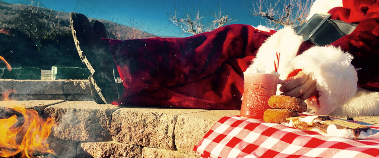 Santa sitting by the firepit with donuts and hot apple cider