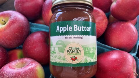 A jar of apple butter lying on red apples