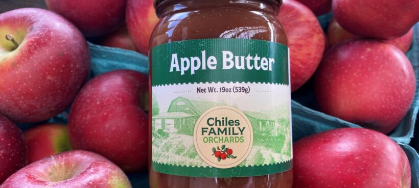 A jar of apple butter lying on red apples