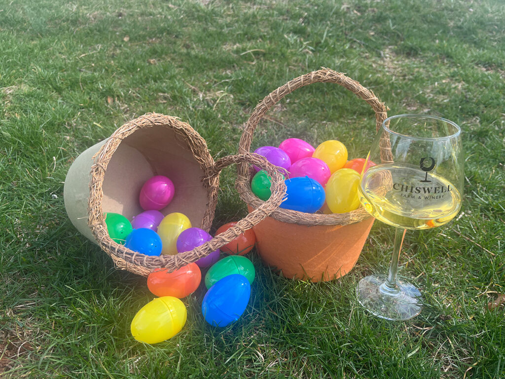 A glass of Chiswell wine next to two baskets of Easter eggs.