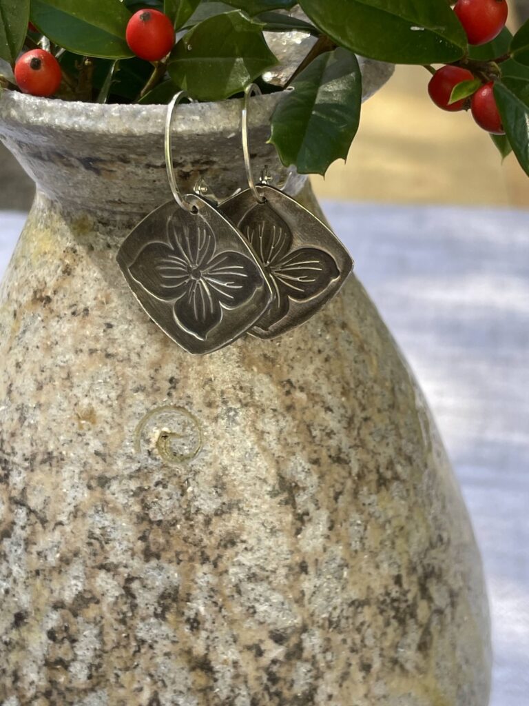 Artisanal metal earrings hanging off a clay planter.