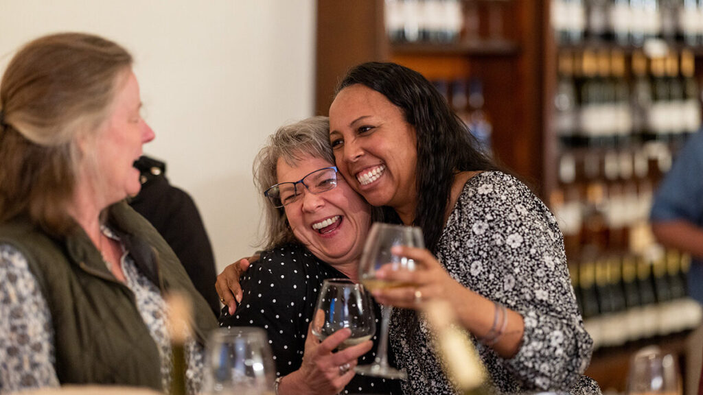 Three women laughing while drinking wine.