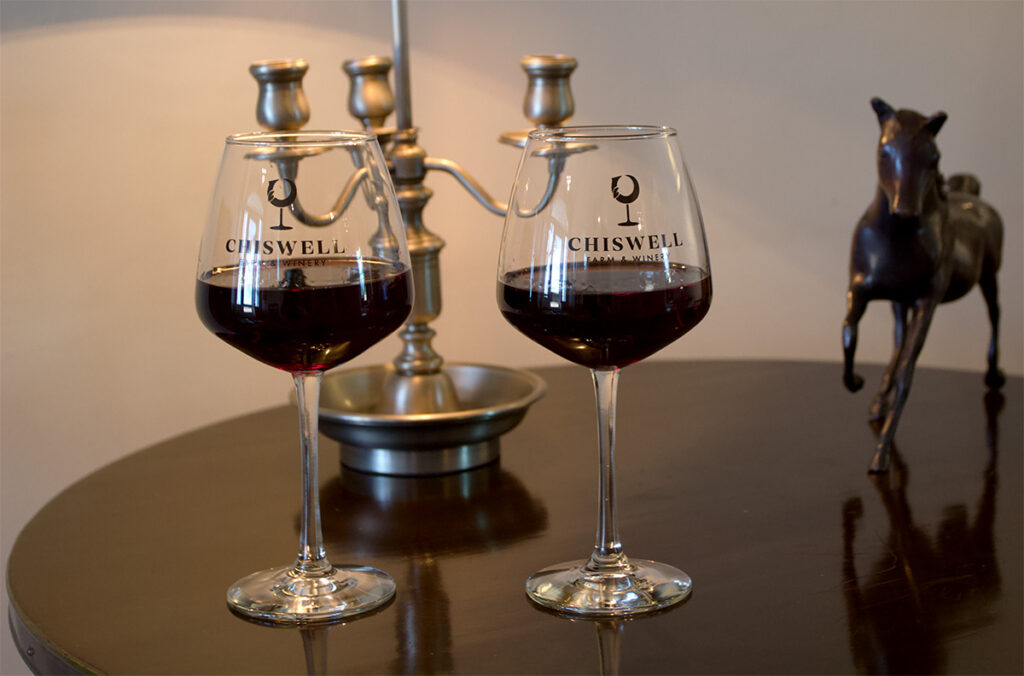 Two Chiswell red wine glasses on a table with a bronze horse and a candlestick.