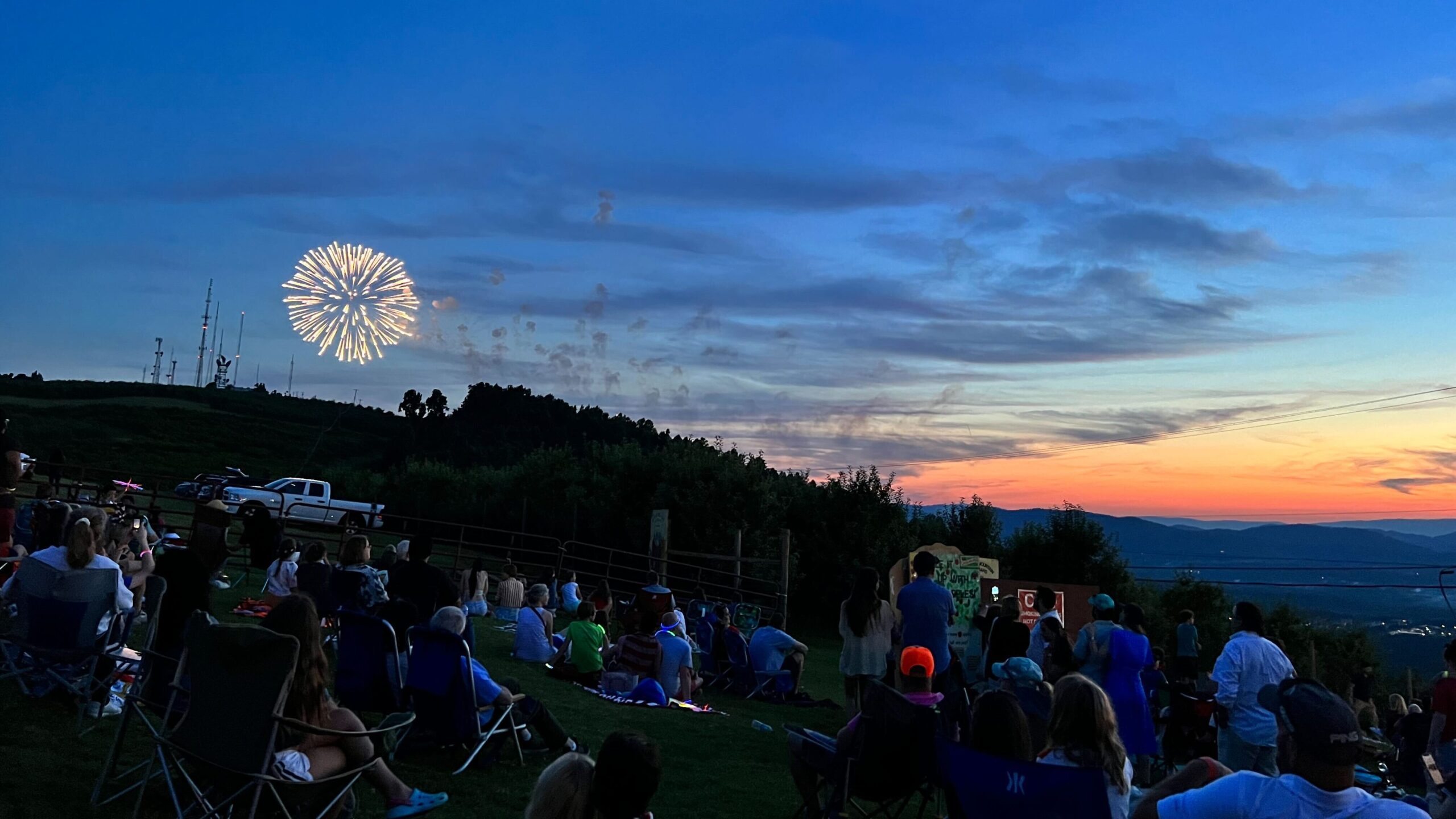 A firework bursting over Carter Mountain as a crowd watches.