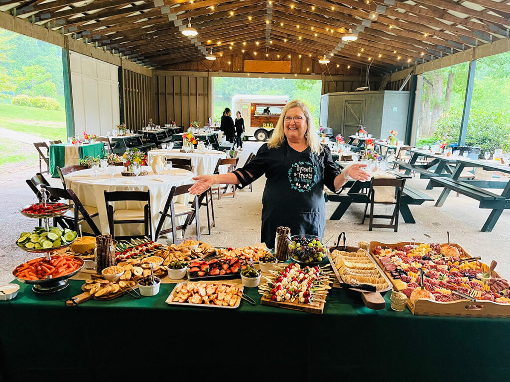 A woman presenting a variety of charcuterie boards at an outdoor event.