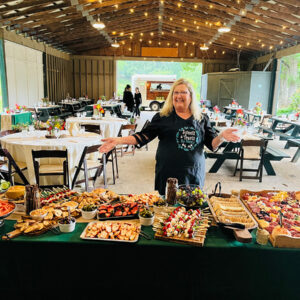 A woman presenting a variety of charcuterie boards at an outdoor event.