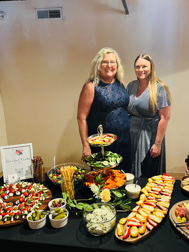 Two women standing behind a spread of charcuterie.