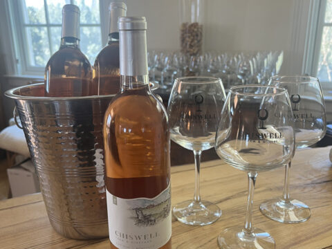 Three bottles of rosé wine next to three wine glasses on a bar