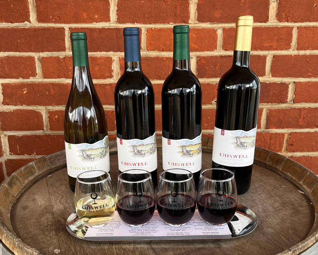 Four wines and four flight glasses in front of a brick wall.