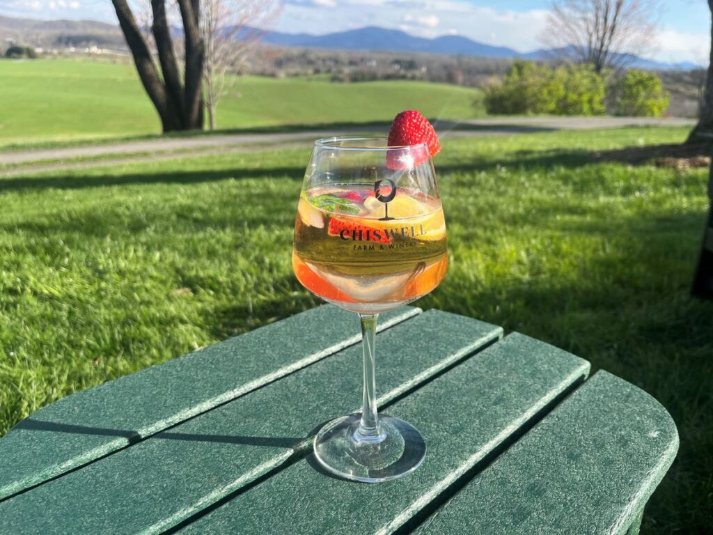 A colorful, fruity spritzer in a wine glass on a table outside.