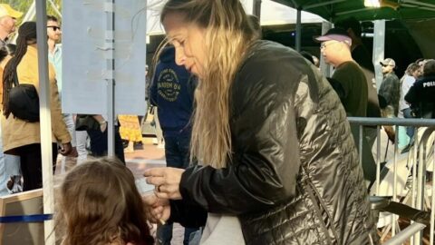 A woman adding tinsel to a seated girl's hair.