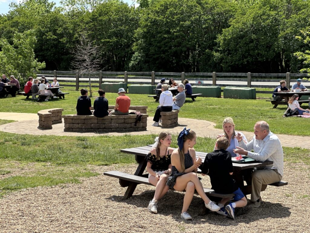 People at tables and a fire pit outdoors in the summer