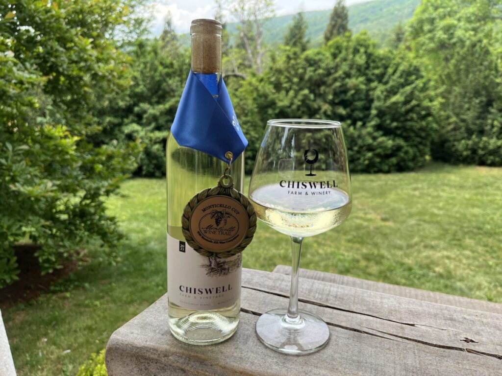 A white wine glass and bottle outdoors, with a gold medal around the bottle.