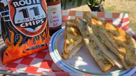 a sandwich, chips, and apple ginger ale bottle on a tray.