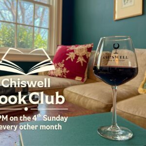 A glass of red wine wine on a table with books.
