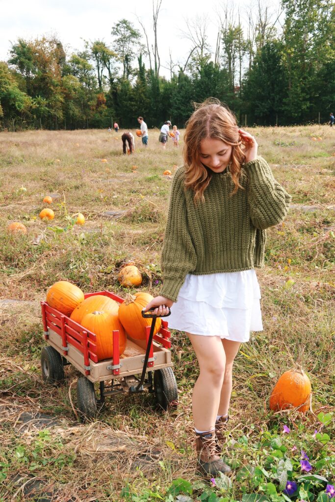 a girl in a pumpkin field pulling a wagon of pumpkins