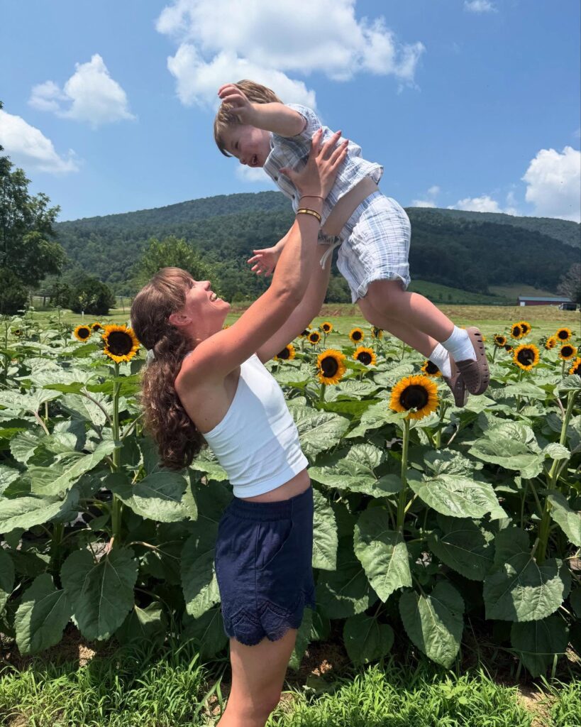 A woman raising a child above a sunflower field