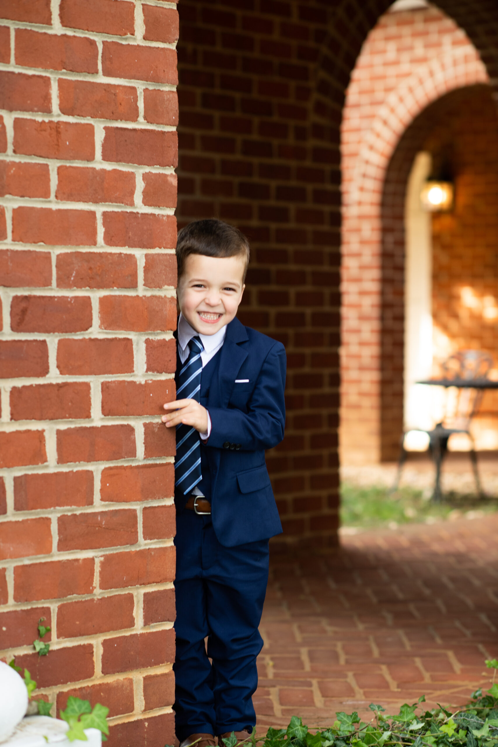 A child in a suit peeking out from behind a brick arch.
