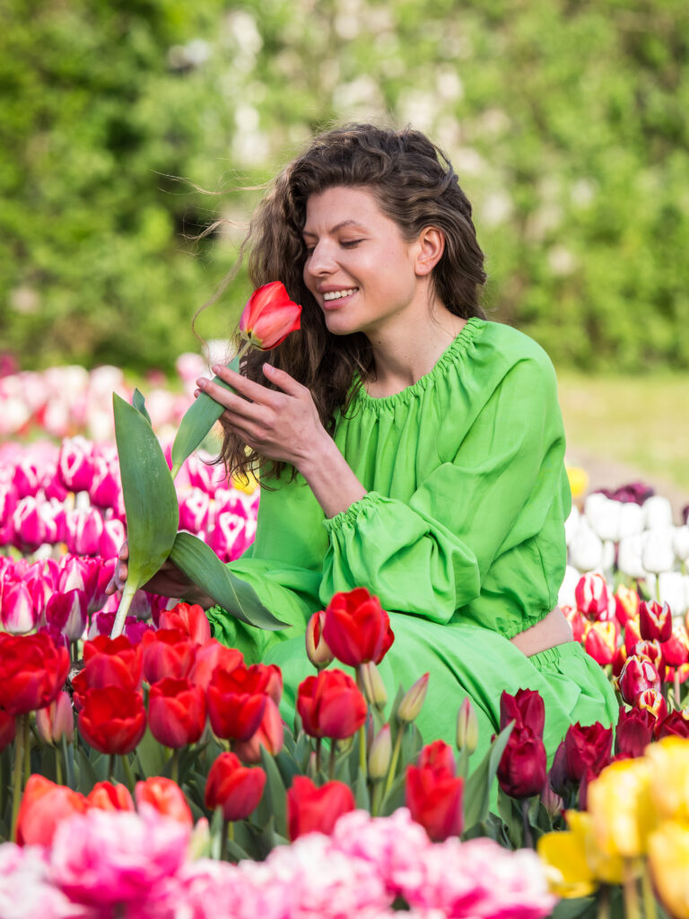 A woman in a tulip field smelling a red tulip