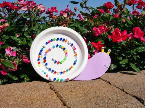 A snail made out of a paper plate and beads