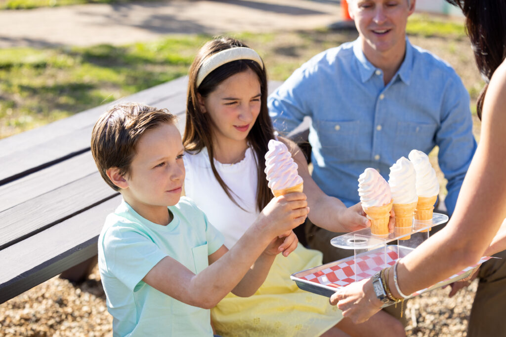 Two children being handed ice cream at a picnic table