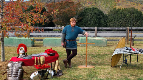 A man outdoors surrounded by Roman arms and armor