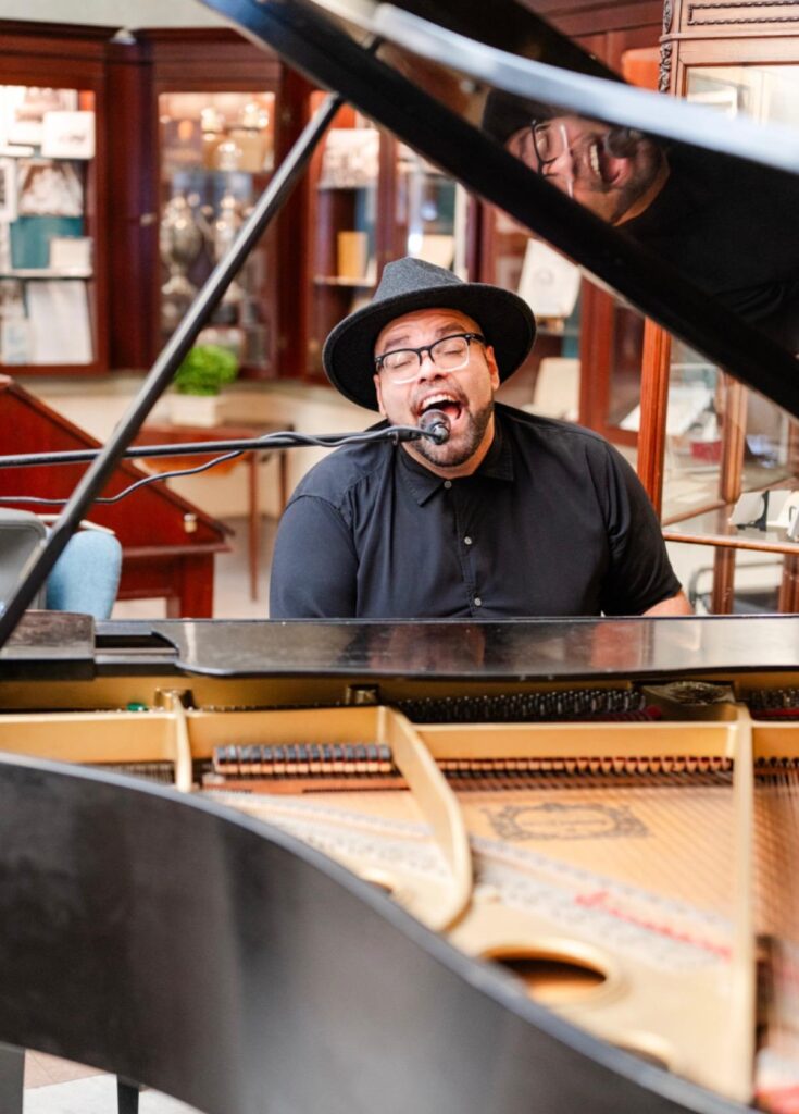 A musician singing into a microphone while playing a grand piano.