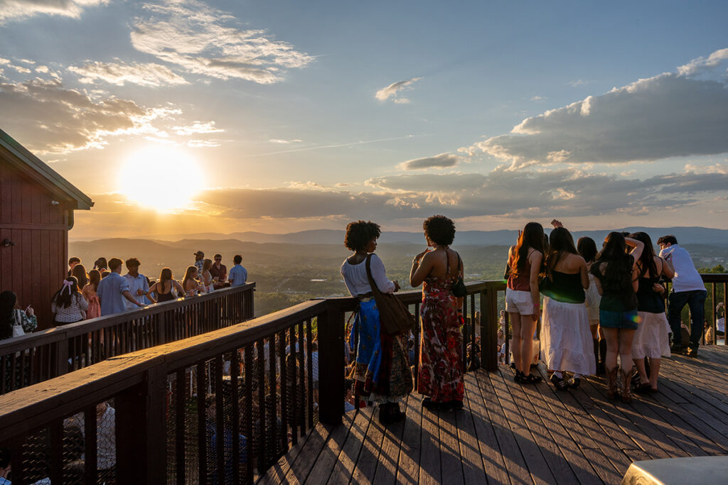 People on wooden decks silhouetted against a mountain sunset