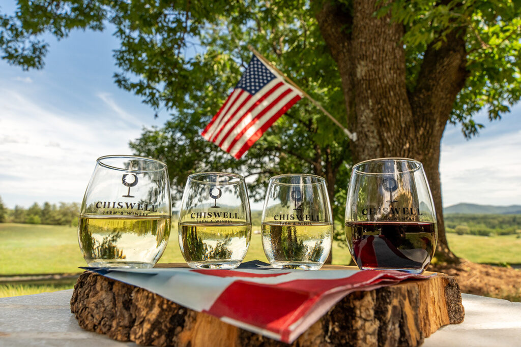 Four wine glasses outside with an American flag in the background