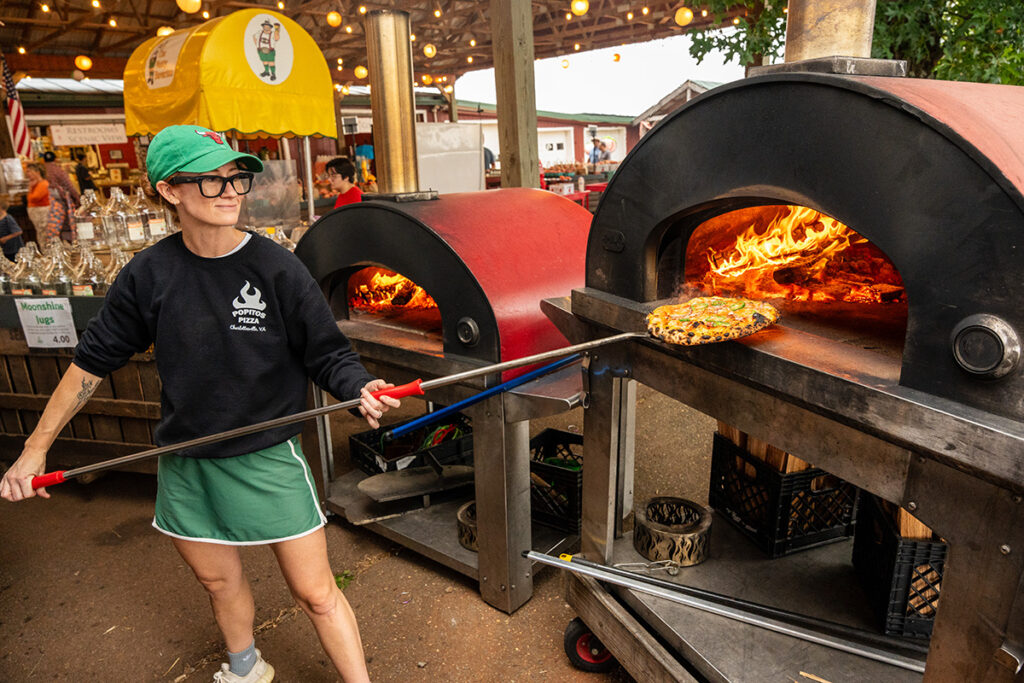 A woman pulling a pizza out of a wood-fired oven