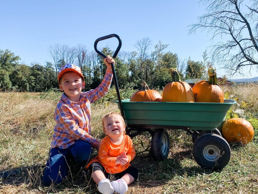 Two kids with a wagon full of pumpkins