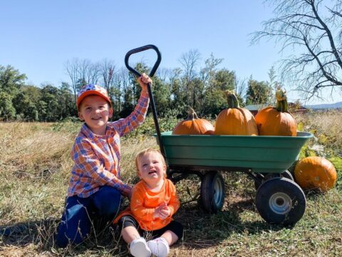 Two kids with a wagon full of pumpkins