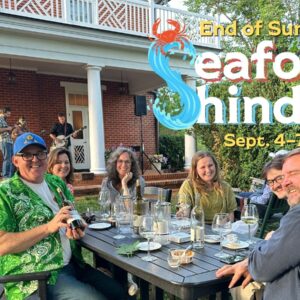 A group of people at a table outdoors at a winery, with the text "Seafood Shindig"