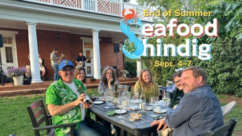 A group of people at a table outdoors at a winery, with the text "Seafood Shindig"