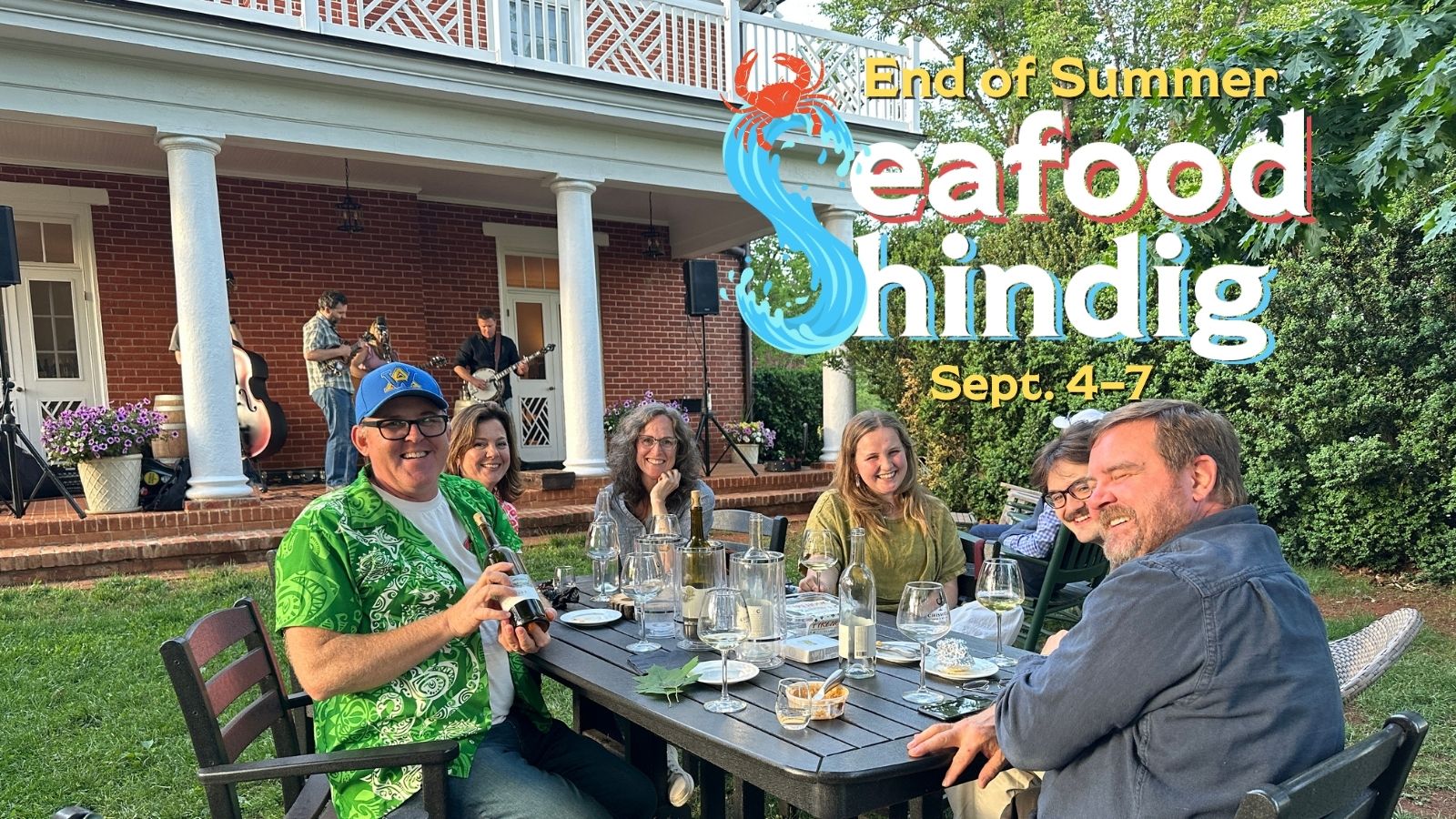 A group of people at a table outdoors at a winery, with the text "Seafood Shindig"