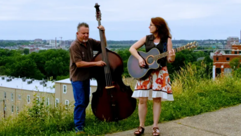 An acoustic guitarist and a stand-up bassist on a hillside